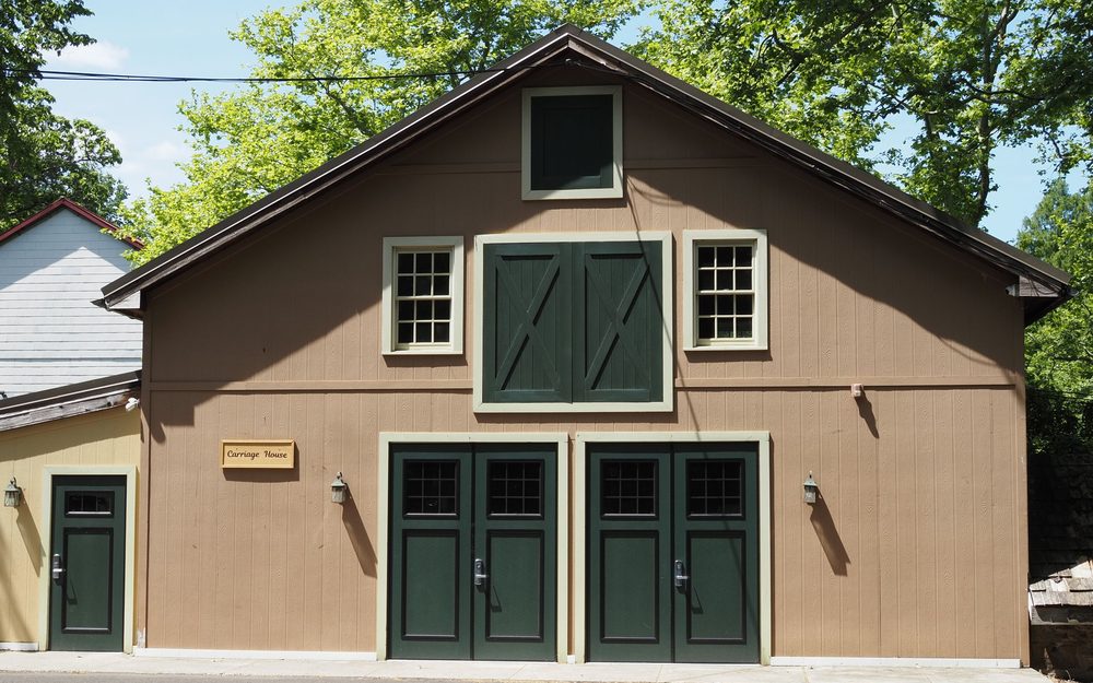 Two-story carriage house with green garage doors on the ground floor and windows on the floor above