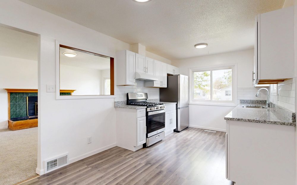 Compact white kitchen with cabinets on two walls, a gas range, a fridge and a window over the sink