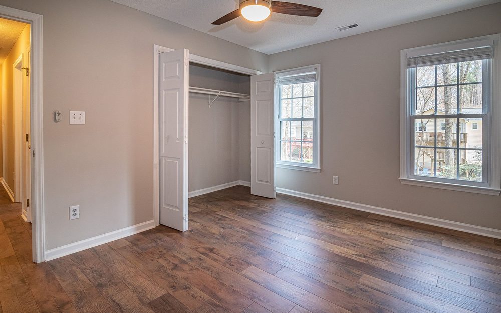 Empty bedroom with wood floors, a ceiling fan, an open closet and two windows