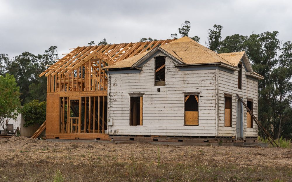 Older white house with new timber framing for an addition rising on one side