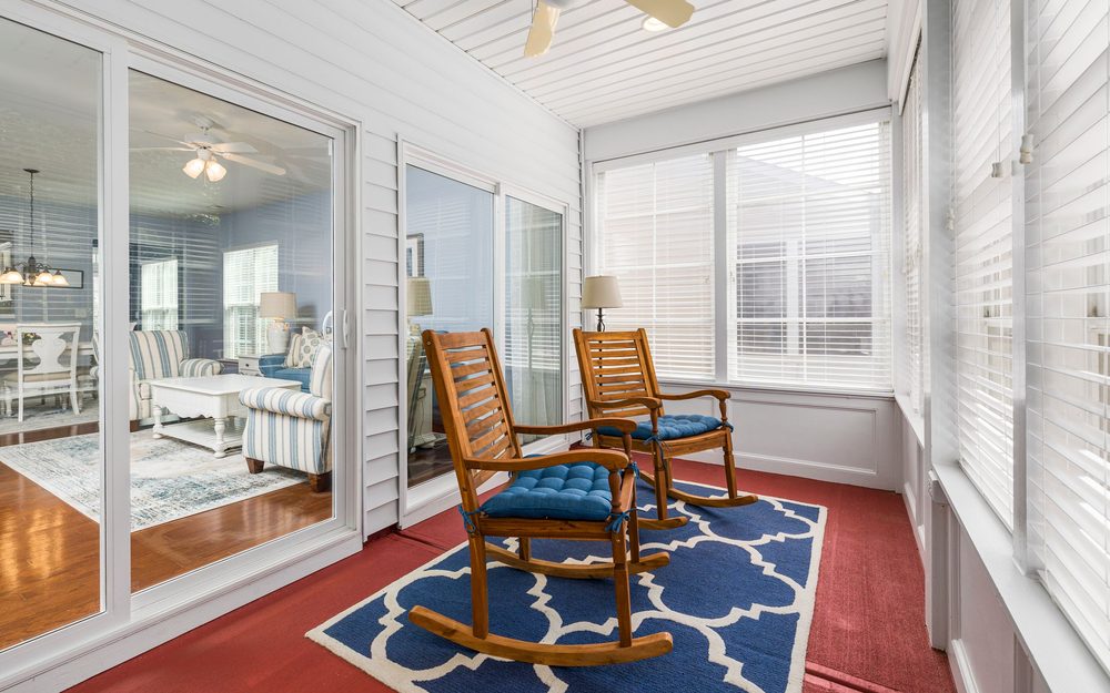 Sunroom with white walls and windows on every side, two wooden rocking chairs on a blue patterned rug