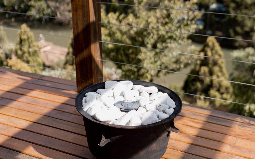 Wooden deck with a thin cable railing and a small fire bowl, looking out over trees and water