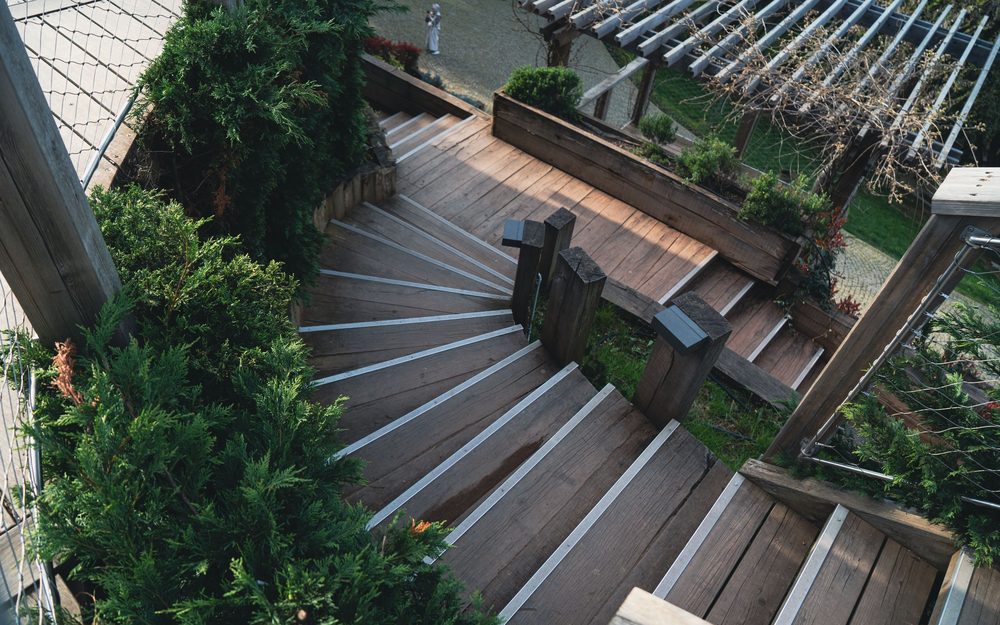 Wooden deck stairs stepping down between planters and greenery, with a bench on a landing