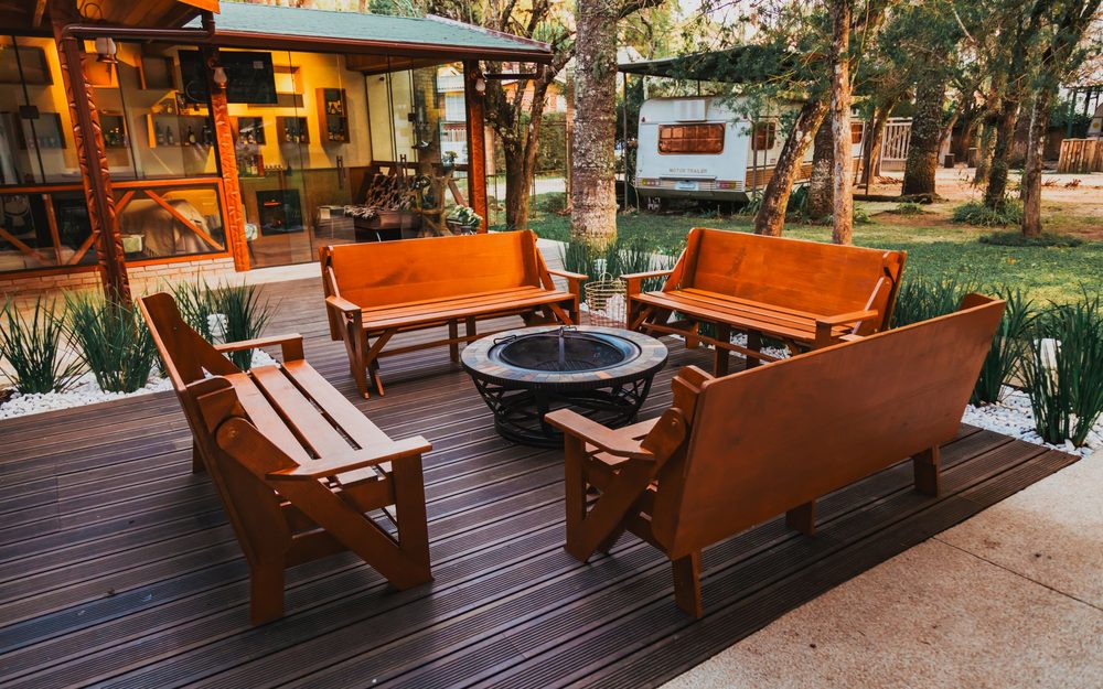 Dark wood deck with four wooden benches arranged around a round fire pit, with trees behind