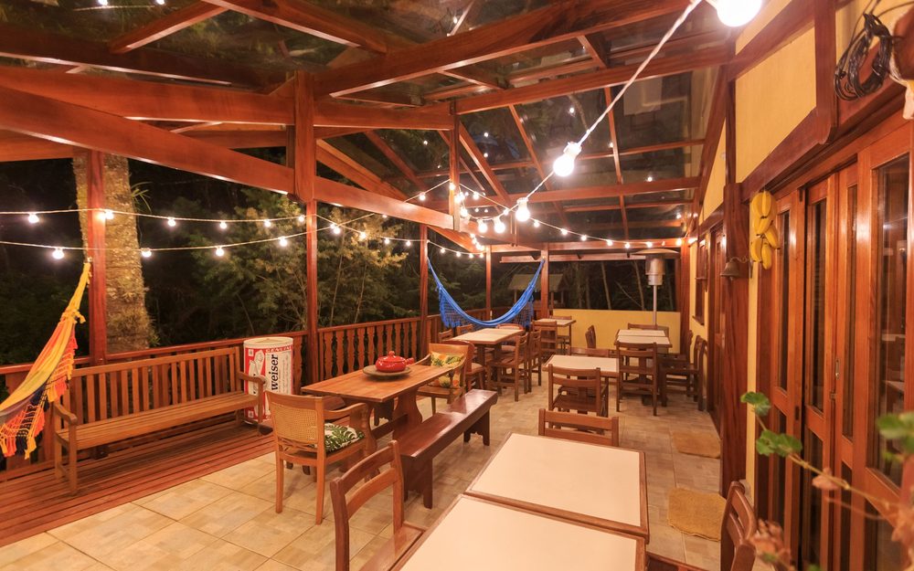 Covered wooden deck at night with string lights overhead, benches, tables and a hammock