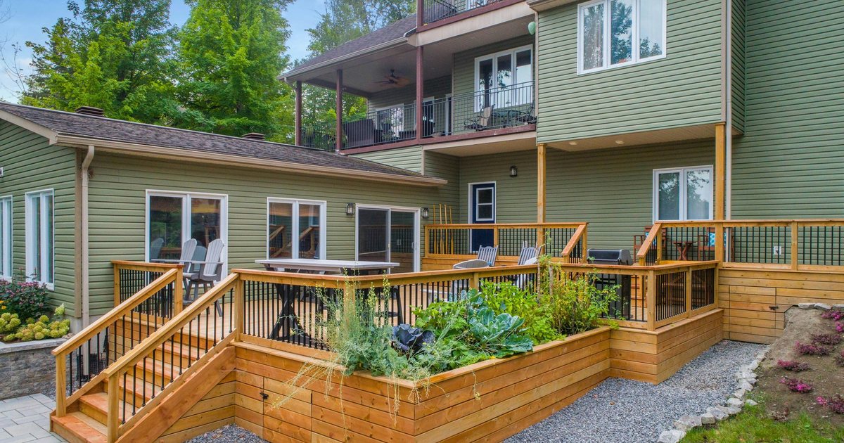 Raised cedar deck with railings and steps behind a green two-story home, backed by Pacific Northwest firs