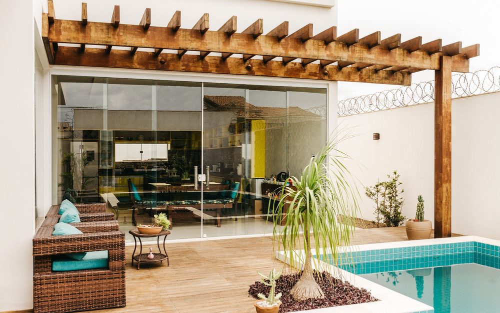 Wooden pergola attached to a modern white house, shading a lounge area beside a pool