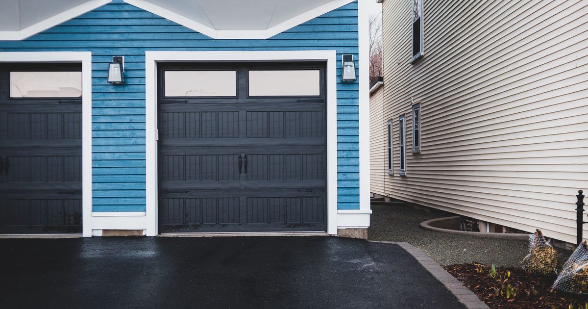 Two dark garage doors in a blue-sided house beside a wet asphalt driveway