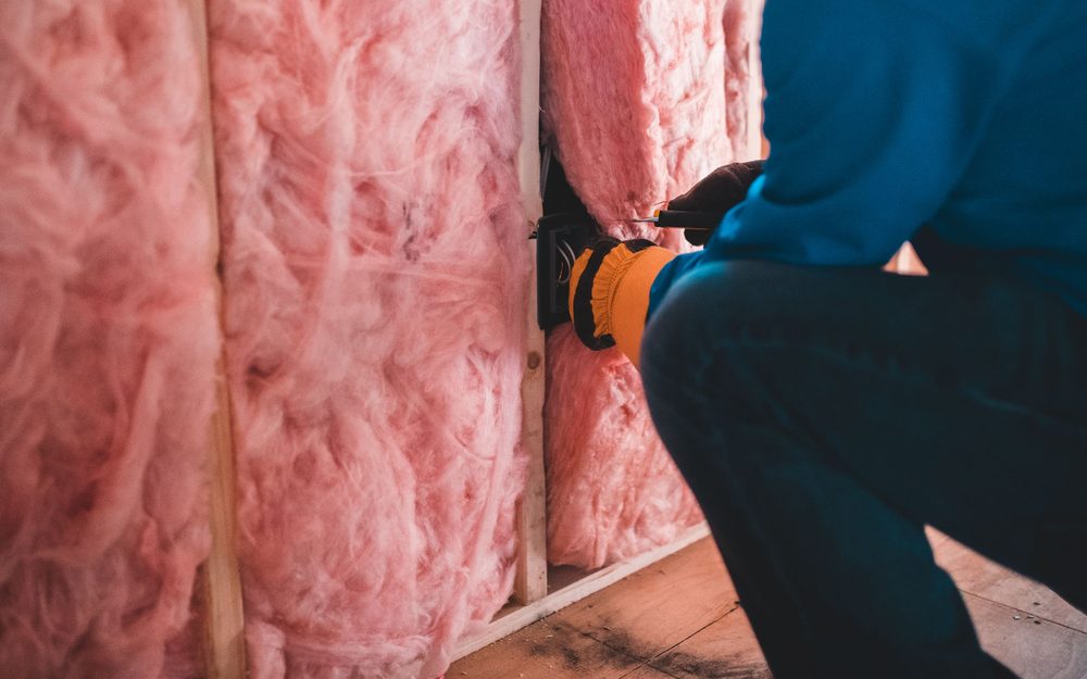 Gloved hand fitting pink insulation between wall studs