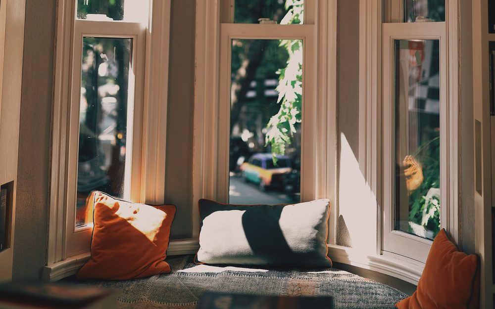 Bay window with a cushioned window seat and pillows, with trees and a street outside