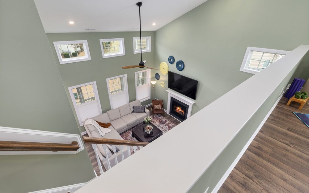 Family room with a vaulted ceiling, high windows, a fireplace and a sofa, seen from an upstairs landing