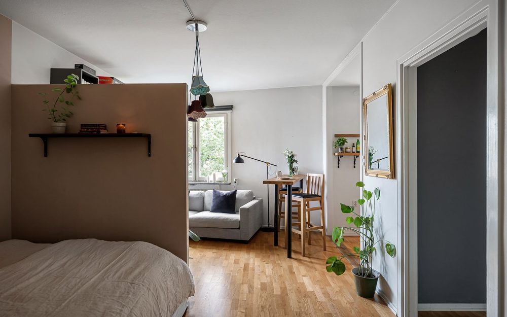 Small suite with a bed behind a half wall, a sofa by the window and a little dining table