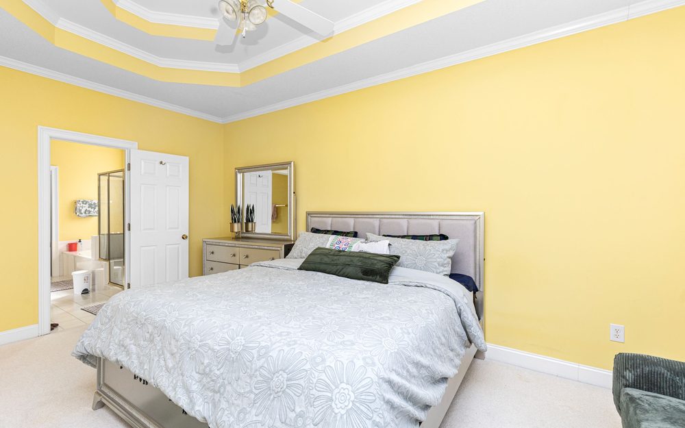 Bright bedroom with a tray ceiling and an open door through to a private bathroom