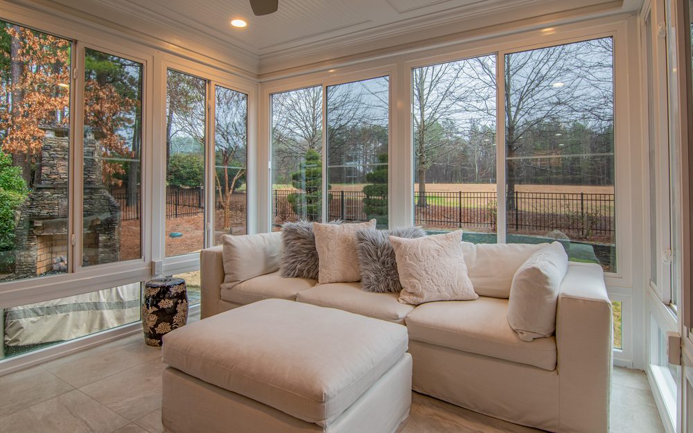 Sunroom with walls of windows looking out on a garden and trees, with a cream sectional sofa