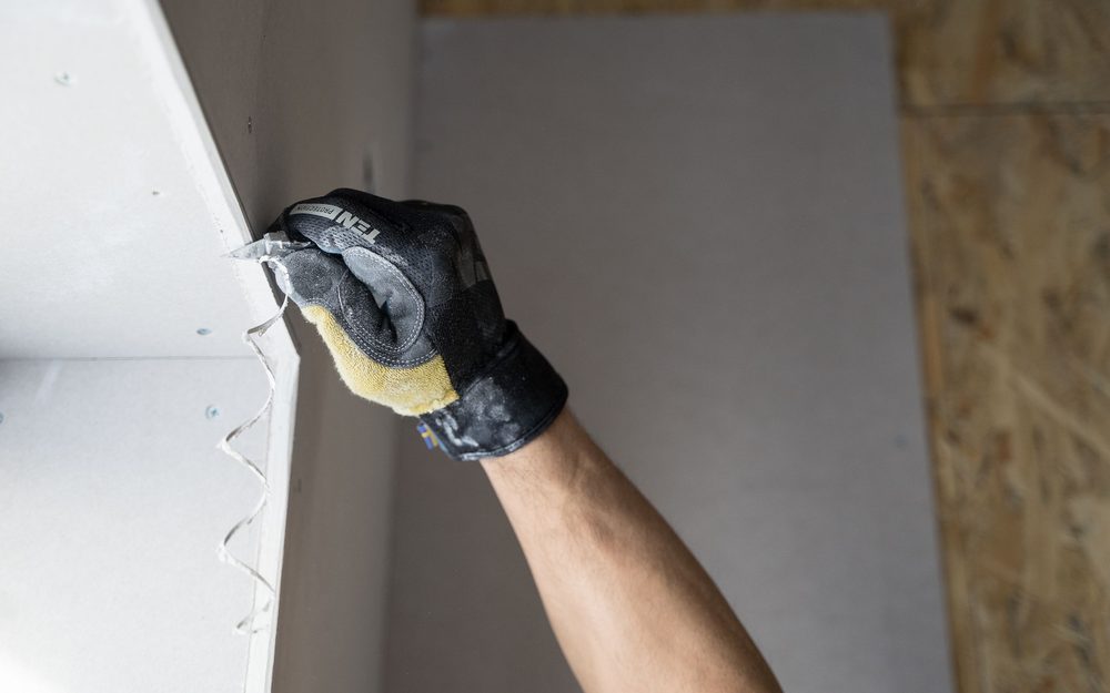 Gloved hand pressing a sheet of drywall into place against a wall