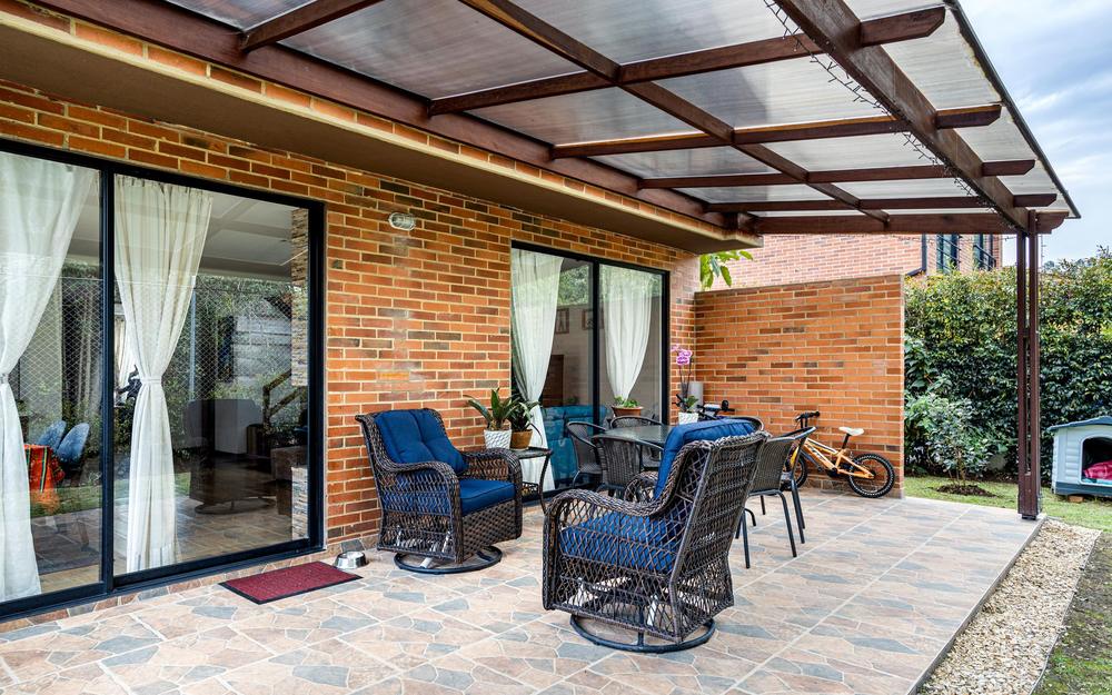 Patio cover with clear roof panels on timber rafters, attached to a brick house over a tiled patio