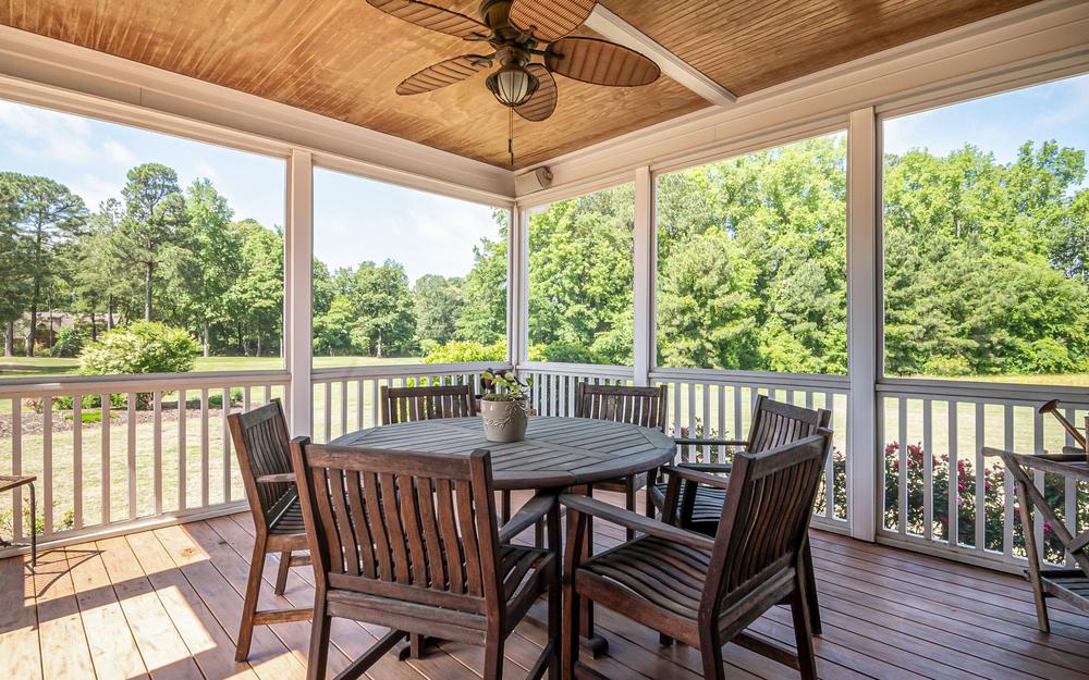 Covered outdoor room with a wood ceiling, a ceiling fan and a dining table overlooking trees