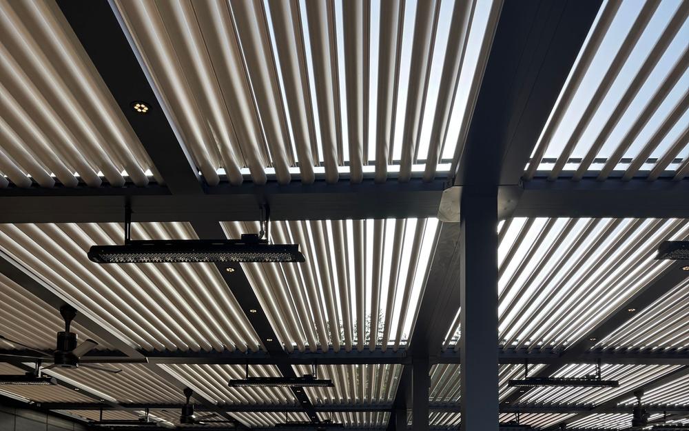 Louvered pergola roof seen from below, with metal slats and heaters mounted under the frame