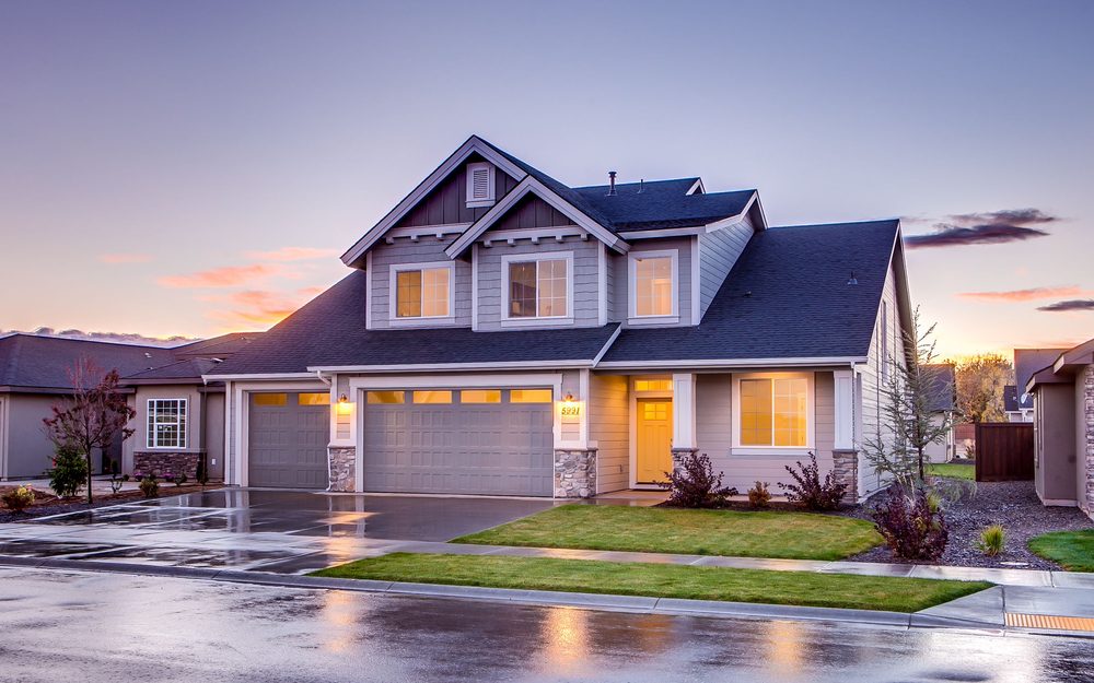 Two-story house with lights on at dusk and a wet, shining driveway and street after rain