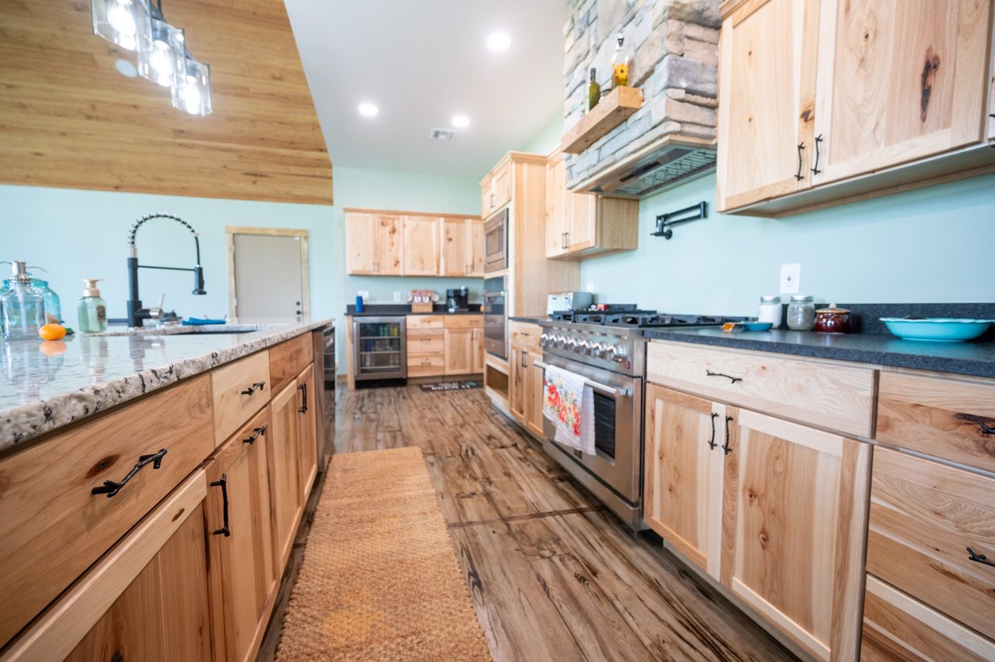 Kitchen with natural hickory cabinets, granite counters, a stone range hood surround and a wood plank ceiling