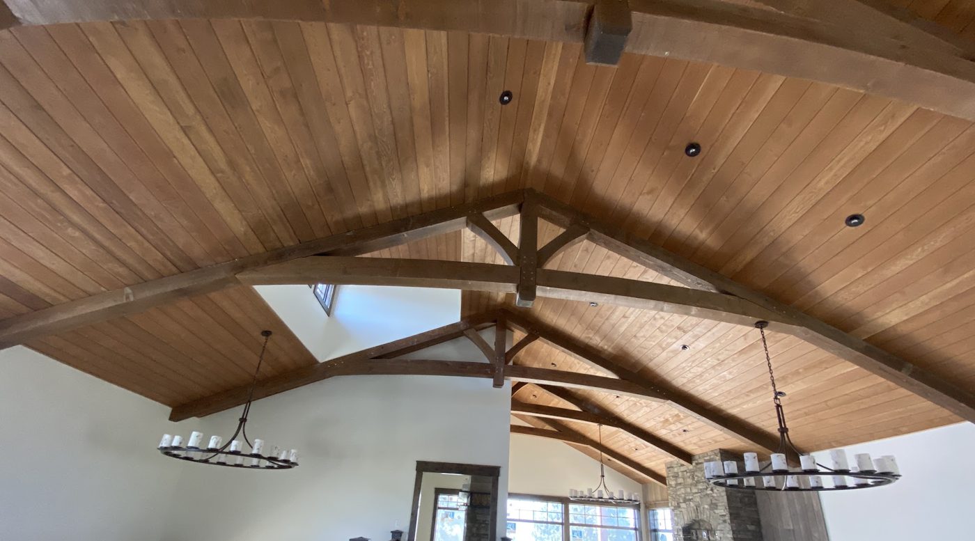 Vaulted ceiling clad in wood planks with exposed timber trusses and iron ring chandeliers