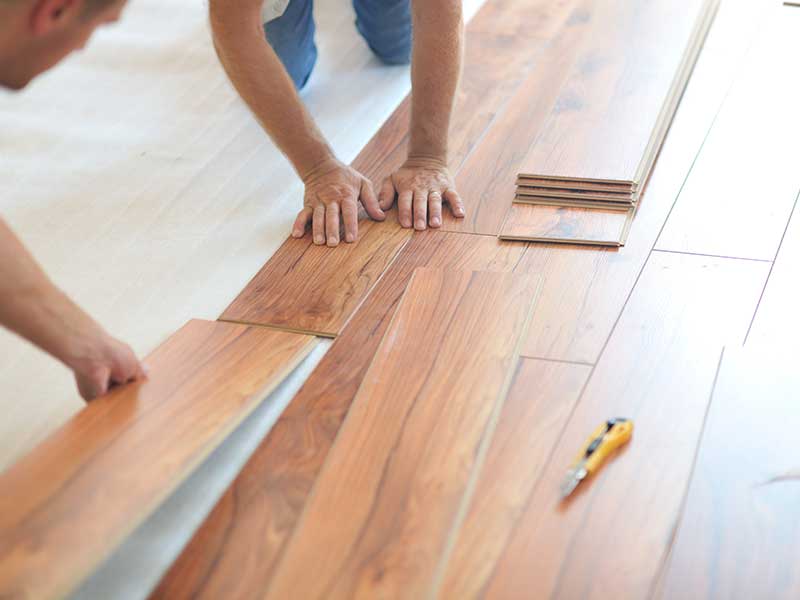 Two men are collaborating on the installation of a wooden floor in a well-lit room.